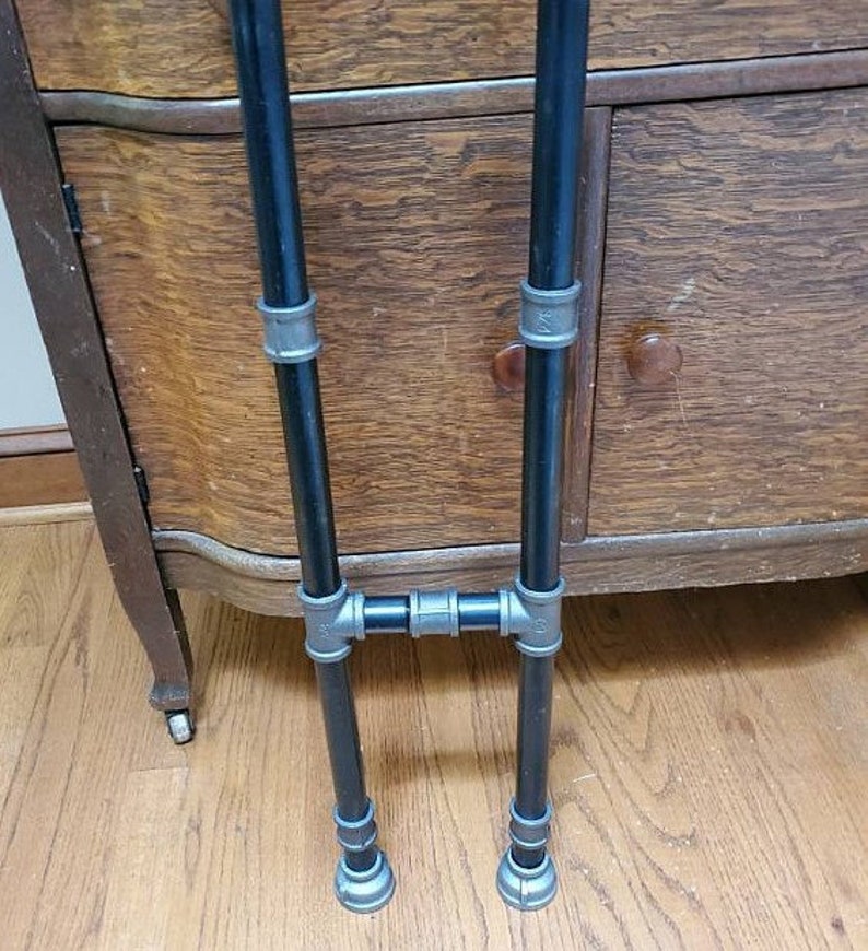 May include: A black metal stand with two vertical pipes and a horizontal connecting pipe. The stand has silver accents on the pipes.