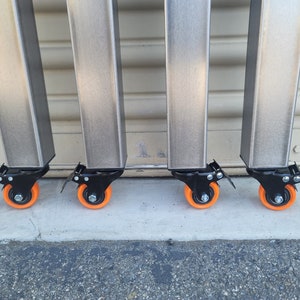 May include: Four silver metal legs with black swivel casters and orange wheels. The legs are attached to a table or other piece of furniture.