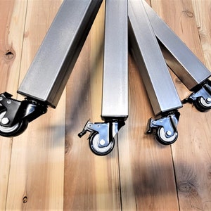 May include: Four silver metal table legs with black caster wheels. The legs are square and have a brushed finish.