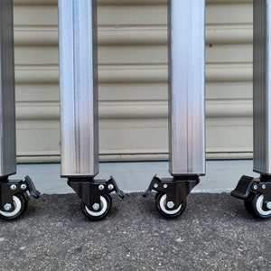 May include: Four silver metal legs with black caster wheels. Each wheel has a brake lever.