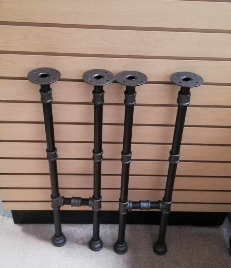 May include: Four black metal pipe table legs with a flange on top. The legs are connected with a cross bar.
