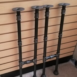 May include: Four black metal table legs with a pipe design. Each leg has a round base and a round top plate.