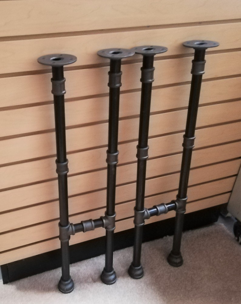 May include: Four black metal table legs with a pipe design. Each leg has a round base and a round top plate.