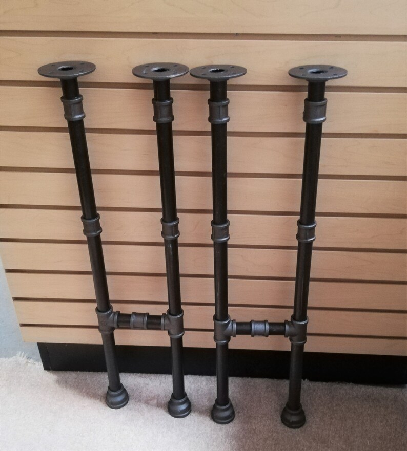 May include: Four black metal pipe legs with flanges on top. The legs are connected with pipe fittings to form a table base.
