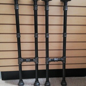 May include: Three black metal pipe table legs with a crossbar. The legs are about 24 inches tall.