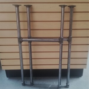 May include: A set of four metal pipe legs for a table or shelf. The legs are made of black metal pipe and have a simple, industrial design.