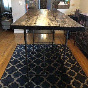 May include: A dark wood table with a black metal frame. The table is on a blue and beige patterned rug. The table is in a room with hardwood floors.