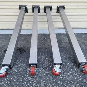 May include: Four silver metal table legs with red wheels. Each leg has a square base and is approximately 24 inches tall.