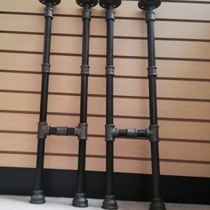 May include: Four black metal pipe legs with flanges on top and bottom. The legs are connected with a crossbar in the middle.