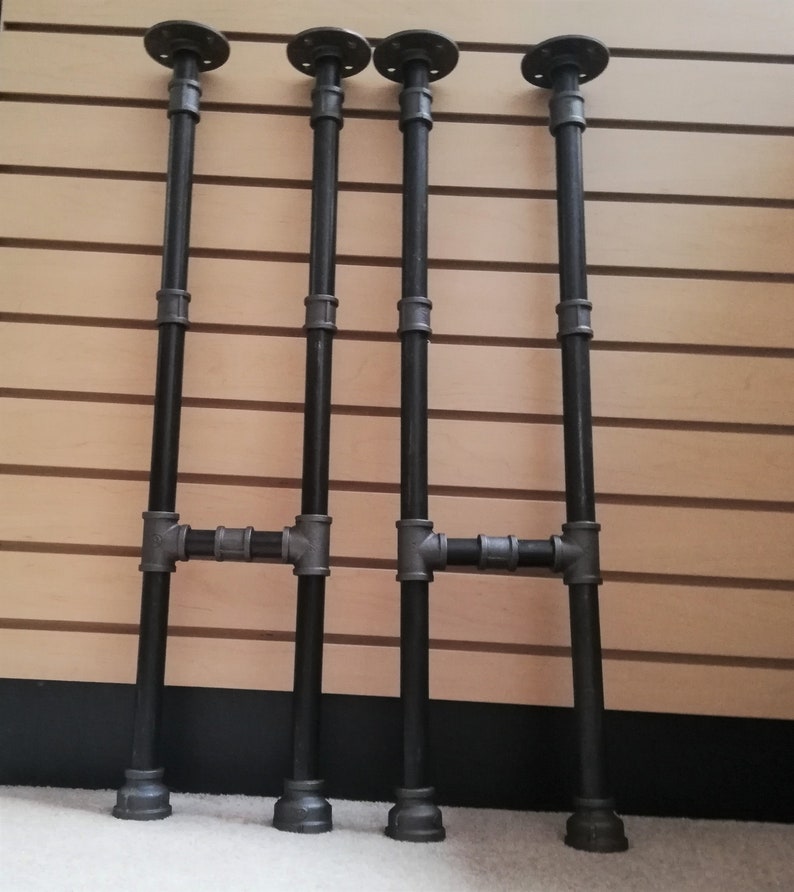 May include: Four black metal pipe legs with flanges on top and bottom. The legs are connected with a crossbar in the middle.