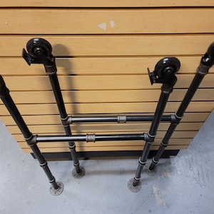 May include: Black metal pipe shelving unit with four wheels. The unit has two shelves and is made of black metal pipe.