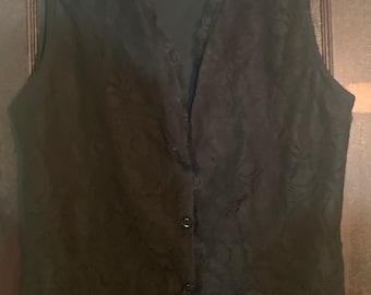 May include: A black sleeveless lace vest with a button closure and a v-neckline. The vest has a delicate floral pattern and the label "remarkable" is visible on the top.