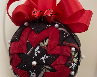 May include: A red and black fabric Christmas ornament with a red bow and bells. The ornament is decorated with white pearl beads.