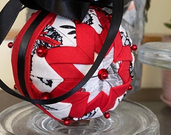 May include: A red and white fabric Christmas ornament with a black ribbon bow. The ornament is decorated with small red beads.
