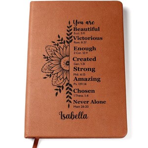 May include: A brown leather journal with a sunflower design and inspirational quotes. The journal has the text "You are Beautiful, Victorious, Enough, Created, Strong, Amazing, Chosen, Never Alone" and the name "Isabella" at the bottom.