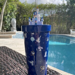 K&ouml;nnte beinhalten: Ein blauer Becher mit einem wei&szlig;en, schlossf&ouml;rmigen Deckel und einem Strohhalm. Der Becher hat ein Muster aus Feuerwerk, Schl&ouml;ssern und der Zahl 50.