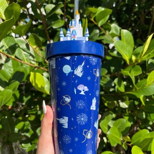 K&ouml;nnte beinhalten: Ein blauer wiederverwendbarer Becher mit einem wei&szlig;en Schlossdeckel und einem Strohhalm. Der Becher hat ein Muster aus wei&szlig;en Schl&ouml;ssern, Feuerwerk und der Zahl 50.