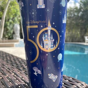 K&ouml;nnte beinhalten: Ein blauer und goldener Becher mit einem 50. Jubil&auml;umsdesign, das das Schloss von Aschenputtel und den Text "Walt Disney World" zeigt.