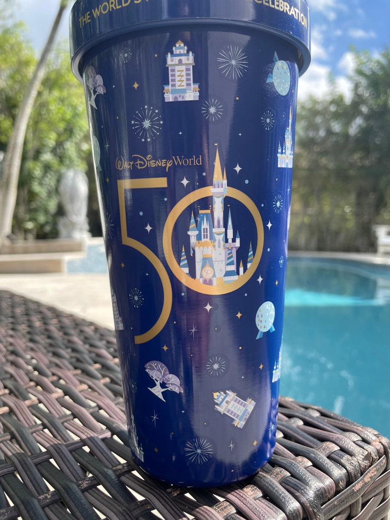 K&ouml;nnte beinhalten: Ein blauer und goldener Becher mit einem 50. Jubil&auml;umsdesign, das das Schloss von Aschenputtel und den Text "Walt Disney World" zeigt.