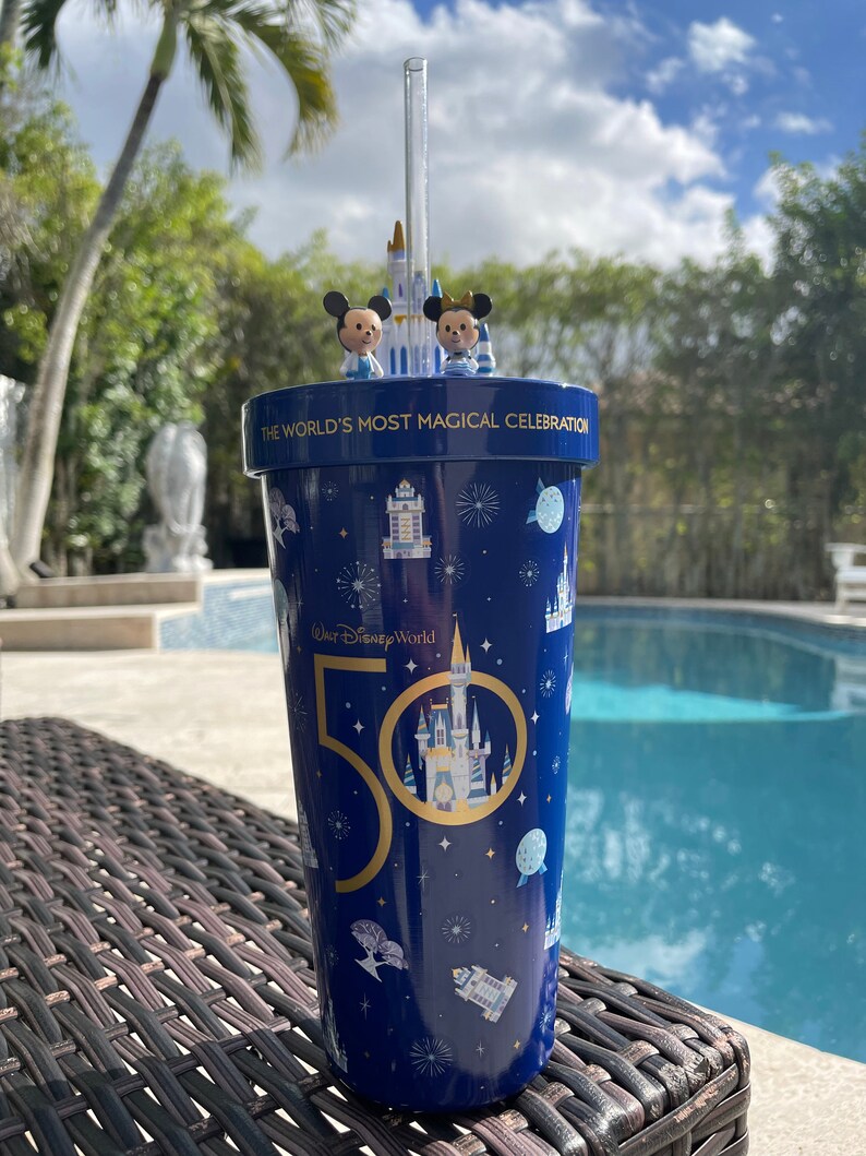 K&ouml;nnte beinhalten: Ein blauer und goldener Becher mit Strohhalm, obenauf Figuren von Mickey Mouse und Minnie Mouse. Der Becher hat ein Design von Schloss Aschenputtel und den Text "The World's Most Magical Celebration" und "Walt Disney World 50".