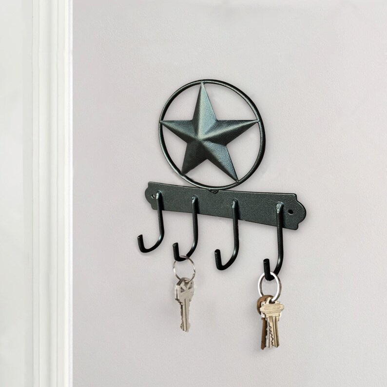 May include: Black metal key holder with four hooks and a star-shaped design. The key holder is mounted on a white wall.