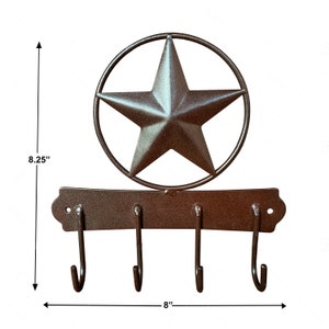 May include: Rustic brown metal key holder with three hooks and a star-shaped design. The star is surrounded by a circle and measures 8.25 inches tall and 8 inches wide.