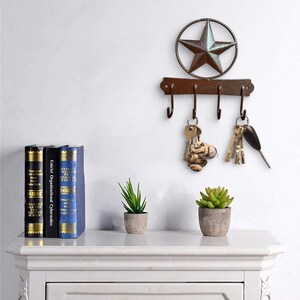 May include: A rustic brown metal key hook with five hooks, a star-shaped design, and a brown wooden shelf with books and plants below.