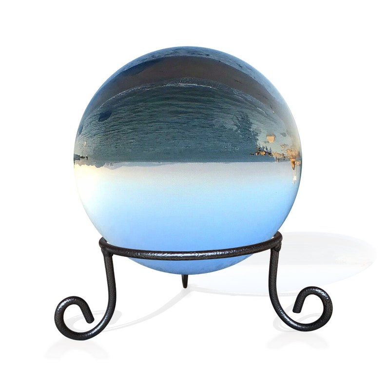 K&ouml;nnte beinhalten: Eine Glaskugel mit einem blauen und wei&szlig;en Bild einer Meereslandschaft im Inneren, die auf einem schwarzen Metallst&auml;nder mit drei Beinen steht.