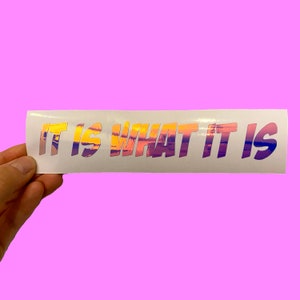 May include: White sticker with the text "IT IS WHAT IT IS" in iridescent letters with a sunset-like pattern.