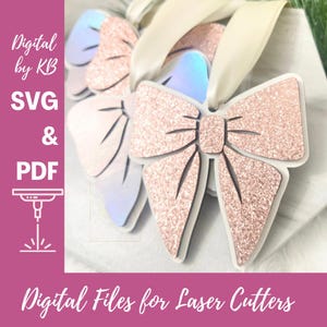 Puede incluir: Archivos digitales SVG y PDF para cortadoras láser. La imagen muestra un conjunto de tres adornos de lazo de brillo rosa con cinta blanca.