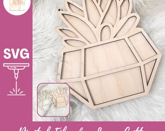 May include: A laser cut wooden geometric succulent planter with a cutout design. The planter is made of light brown wood and has a geometric shape with a cutout design in the center. The planter is perfect for displaying succulents or other small plants.