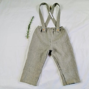 May include: Green and white striped linen pants with adjustable suspenders. The suspenders have a criss-cross design and are secured with brown buttons.