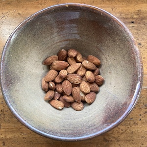 May include: A brown ceramic bowl filled with a pile of almonds.