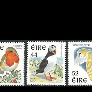 May include: A collection of Irish postage stamps featuring various birds. The stamps showcase a blue tit, a robin, a puffin, a barn owl, and a Greenland white-fronted goose. Each stamp has a denomination in the upper right corner.