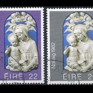 May include: Two vintage Irish Christmas stamps featuring a depiction of the Virgin Mary and baby Jesus. The stamps are from 1982 and have a purple and gray background. The text "Noilaig 1982" is printed on both stamps. The stamp on the left has a denomination of 22 and the stamp on the right has a denomination of 26.