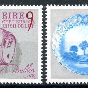 May include: Two vintage Irish postage stamps featuring a pink and white ceramic barrel and a blue and white ceramic plate with a lace border. The stamps are from the 1960s and feature the text "EIRE" and "CEPT EUROPA IRISH DELFT".
