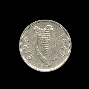 Puede incluir: Una moneda irlandesa de color plateado que presenta un arpa en el centro, con la palabra "eire" impresa en el lado izquierdo y el año "1940" en el lado derecho. La moneda tiene forma circular con un borde de cuentas en el exterior.