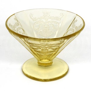 May include: A yellow glass dessert dish with a footed base and a delicate etched floral design.