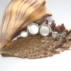 May include: A set of four silver cufflinks with white mother-of-pearl inlays. The cufflinks are arranged in a row on a seashell.