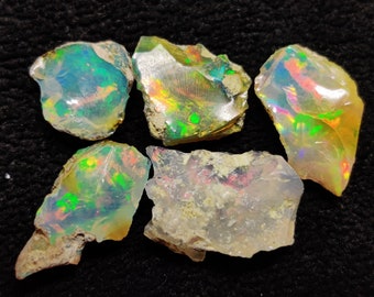 May include: Five rough-cut pieces of opal, with iridescent colors of green, blue, and yellow, on a black background.