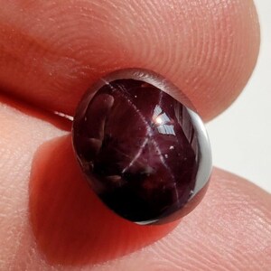 May include: A deep red star ruby cabochon gemstone with a six-rayed star.