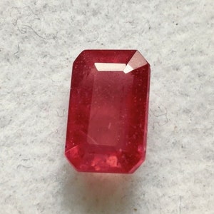 May include: A deep red gemstone with a rectangular emerald cut.