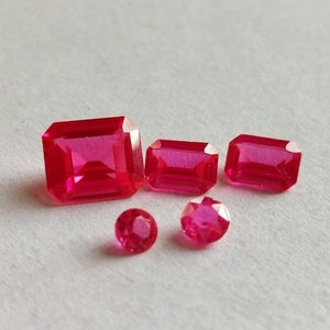 Op de afbeelding: Vier roze, gefacetteerde, rechthoekige edelstenen in verschillende maten. De grootste edelsteen is ongeveer 2,5 cm lang. De edelstenen zijn in een rij op een wit oppervlak gerangschikt.