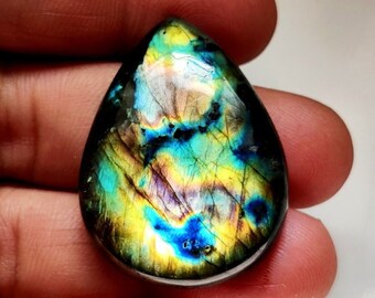 May include: A teardrop-shaped labradorite gemstone cabochon with iridescent blue, green, and gold colors.