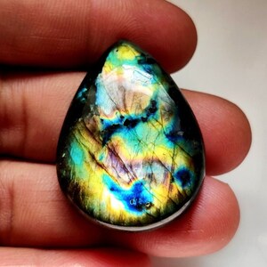 May include: A teardrop-shaped labradorite gemstone cabochon with iridescent blue, green, and gold colors.