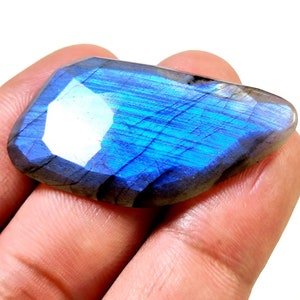 May include: A large, iridescent blue labradorite gemstone with a faceted cut. The stone has a dark gray base with blue and green flashes of color.