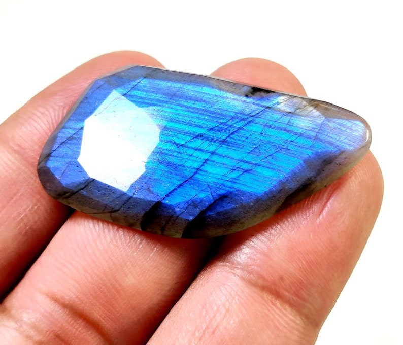May include: A large, iridescent blue labradorite gemstone with a faceted cut. The stone has a dark gray base with blue and green flashes of color.