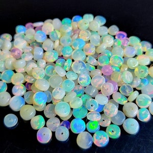 May include: A large pile of iridescent opal beads, each bead is a light, milky white with flashes of rainbow colors. The beads are round and flat, with a hole drilled through the center.