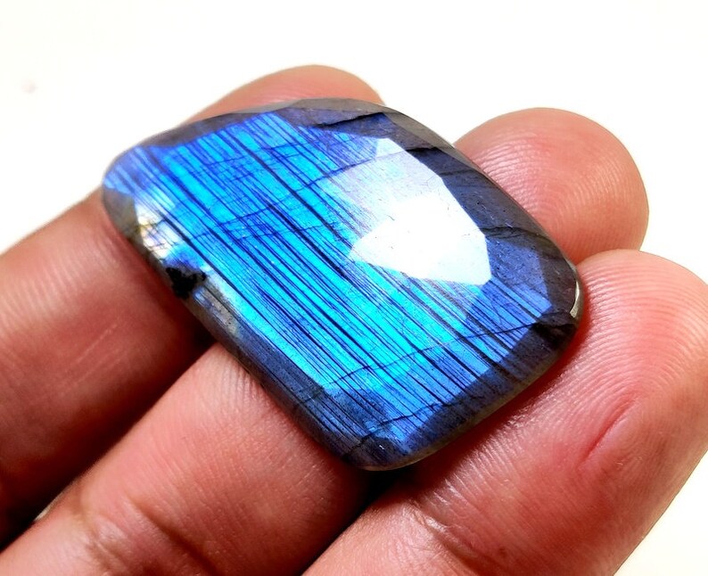 May include: A large, iridescent blue labradorite gemstone with a rectangular shape. The stone has a unique, shimmering effect that is characteristic of labradorite.