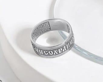 May include: A silver-colored ring with engraved text around the band. The ring has a polished finish and is set against a white background. The text appears to be in a foreign language.